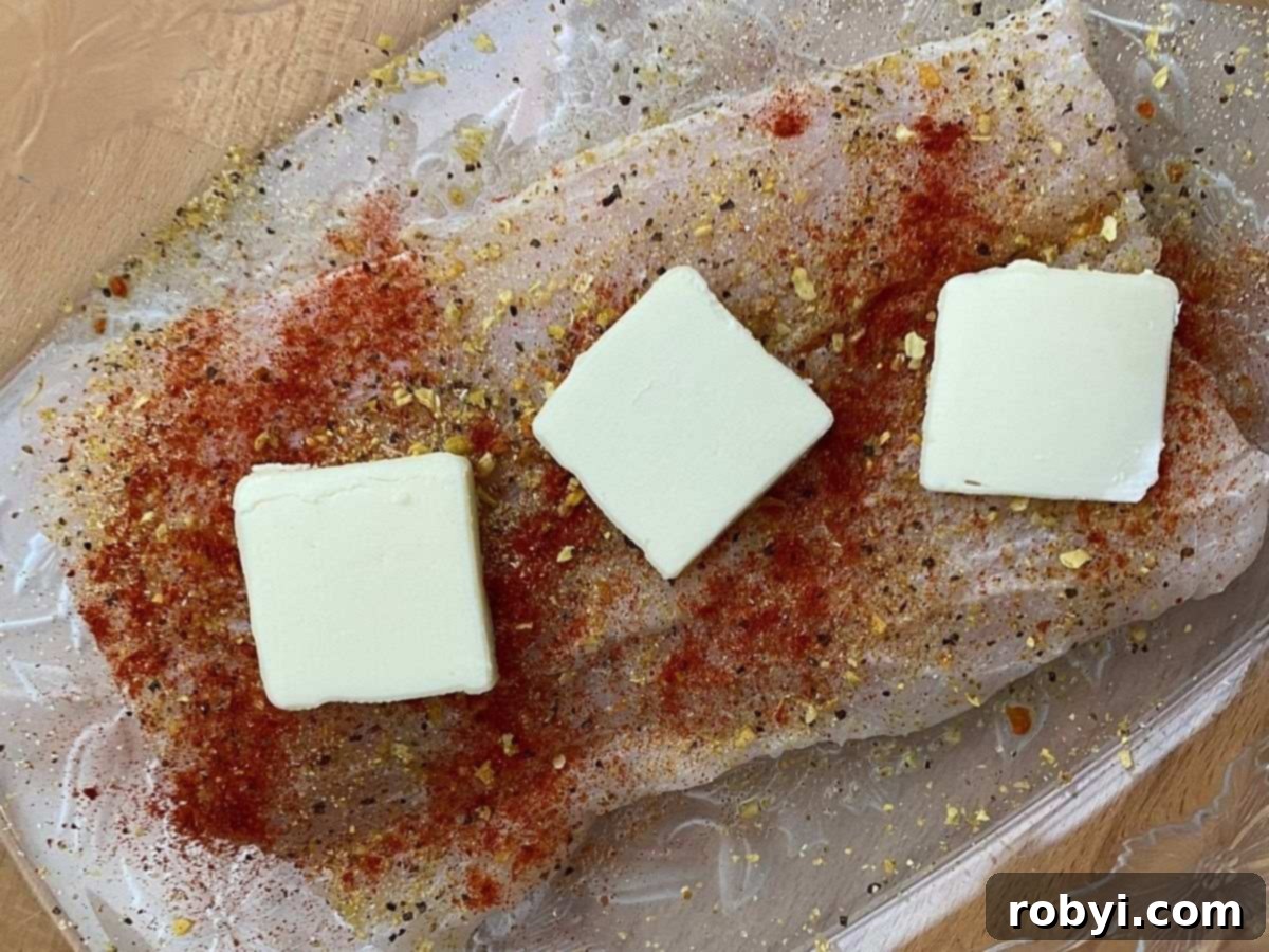 Uncooked corvina fillet with seasonings and butter in baking dish.