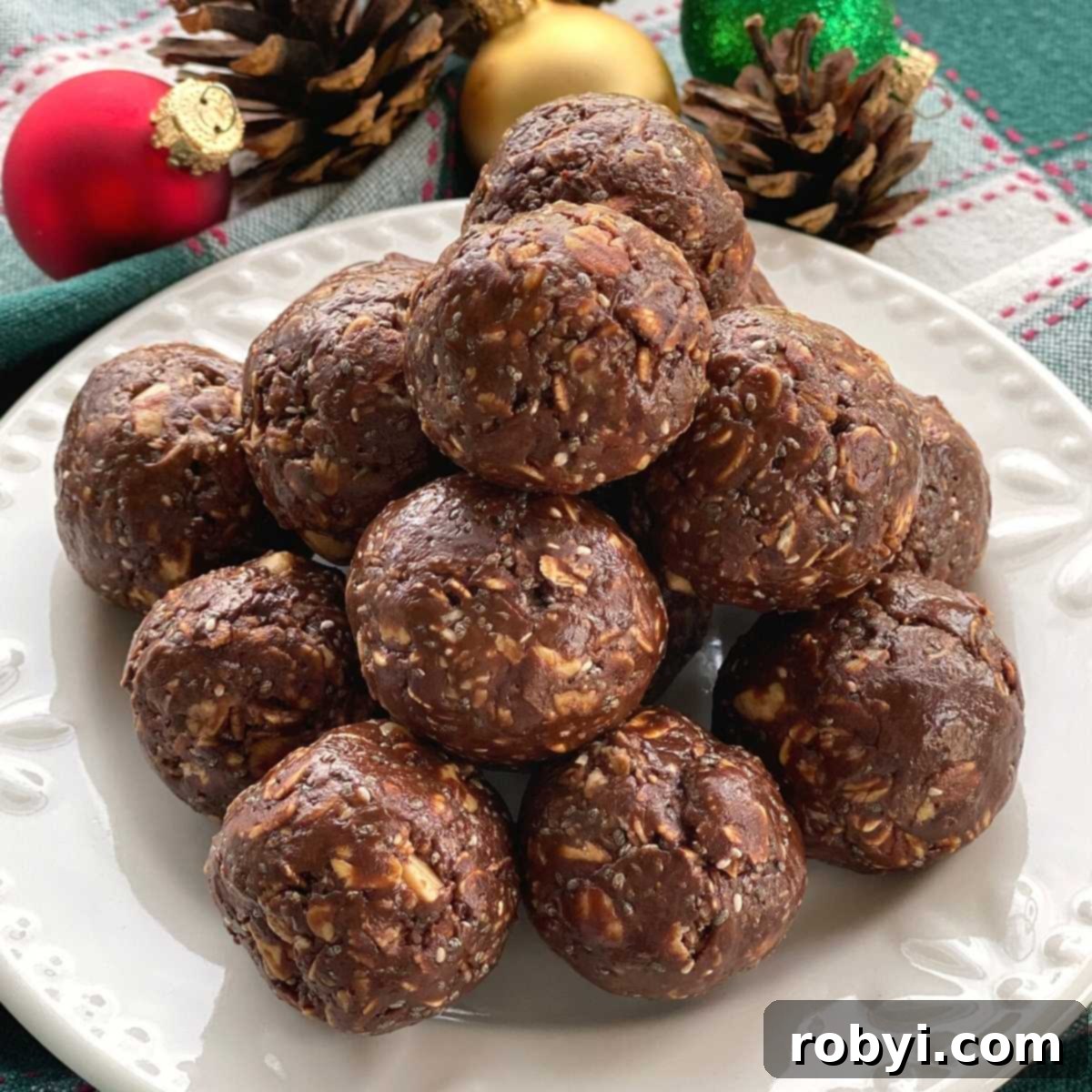A vibrant plate of Chocolate Bliss Balls made with hot honey, artfully arranged with festive pine cones and holiday ornaments in the background, suggesting a perfect seasonal treat.