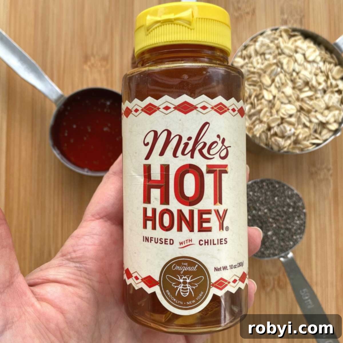 A hand confidently holds a bottle of Mike's Hot Honey, highlighting the popular brand used in this recipe and its recognizable packaging.