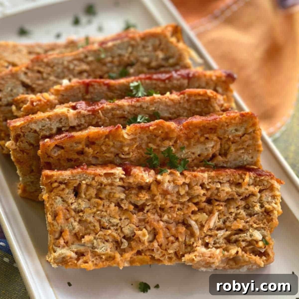 Slices of juicy ground chicken meatloaf garnished with fresh parsley on a serving platter, indicating a wholesome and flavorful meal.