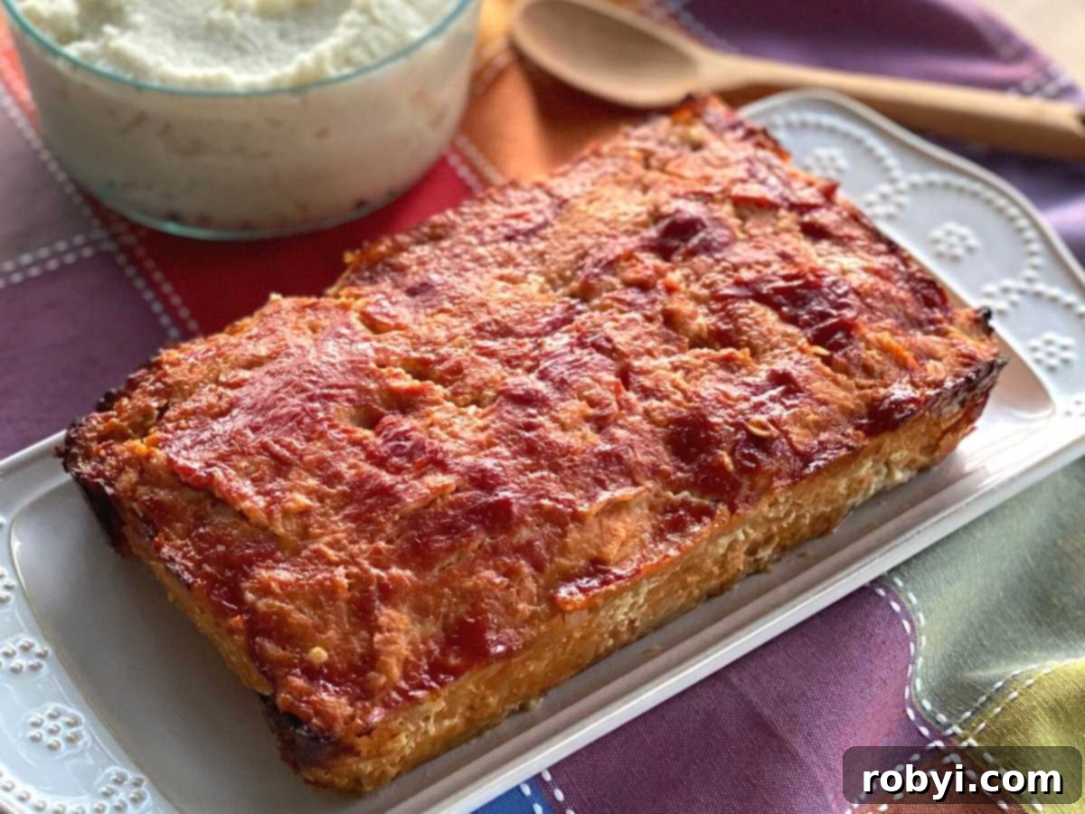 Generous slices of ground chicken meatloaf served on a platter, with a bowl of creamy mashed potatoes in the background, ready for a comforting meal.