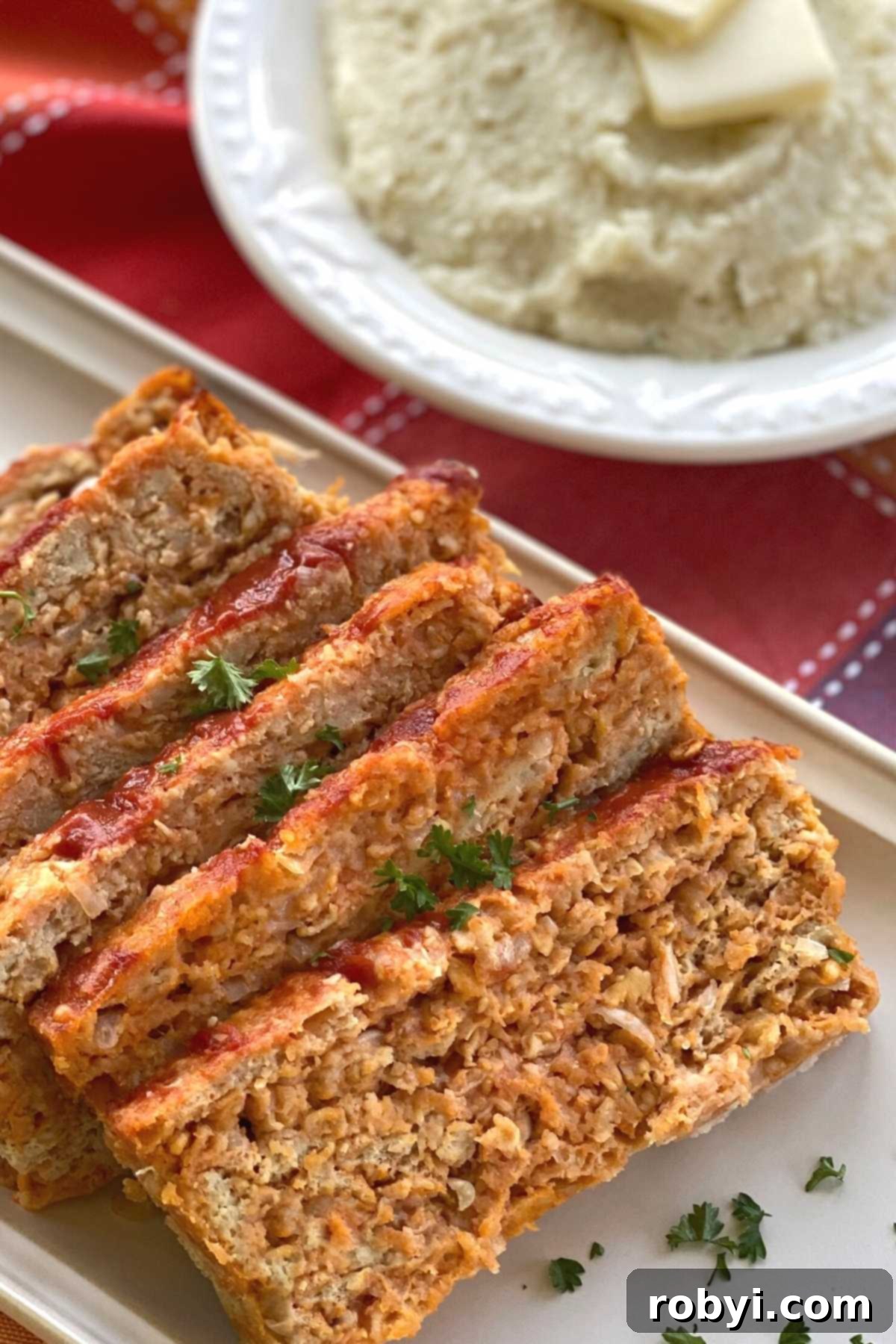 Slices of chicken meatloaf on a platter next to a bowl of creamy cauliflower mash, illustrating a balanced and delicious meal.