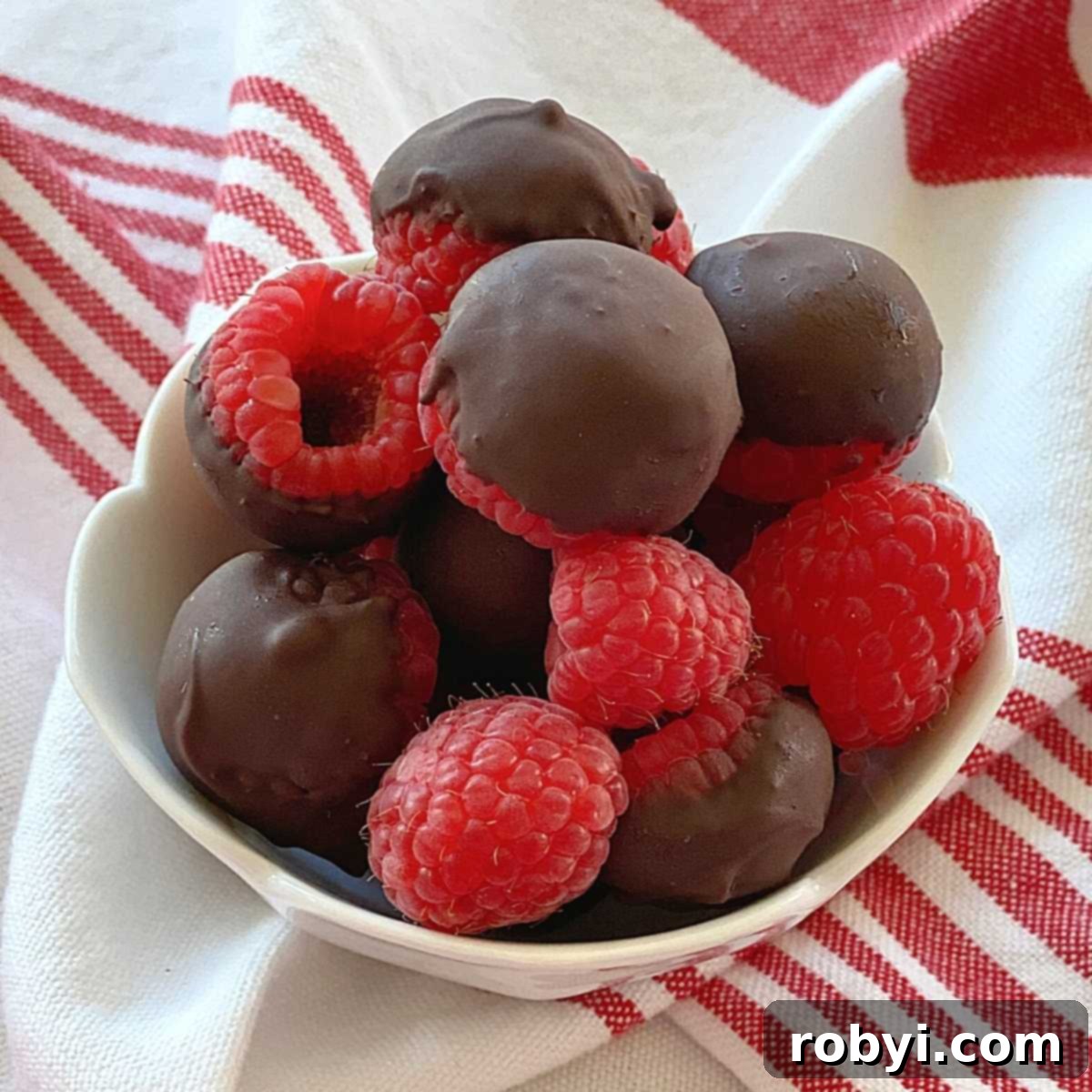 Chocolate-Dipped Frozen Raspberry Jewels 2 A bowl brimming with glistening frozen chocolate covered raspberries, alongside a few fresh, undipped raspberries, ready for a healthy, low-carb treat.