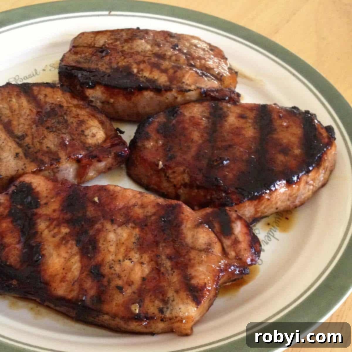 Four perfectly grilled pork chops glazed with molasses marinade on a serving plate.