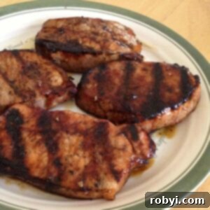 Four pork chops coated with molasses marinade on a plate, ready for grilling.