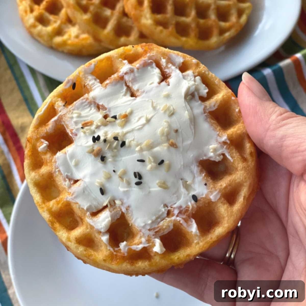 Hand holding a savory keto chaffle smeared with cream cheese.