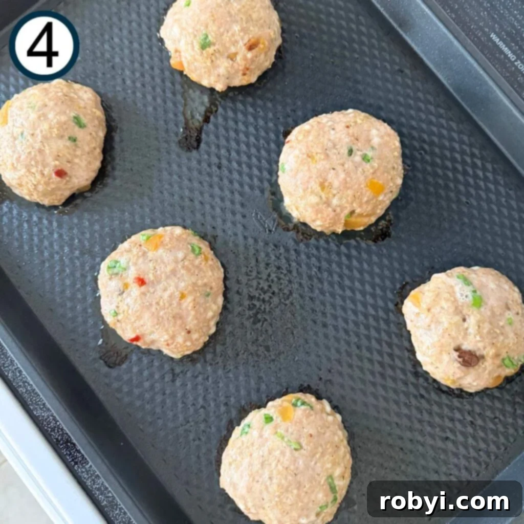 Six turkey burgers on a baking sheet that after they have cooked on one side and been flipped over.