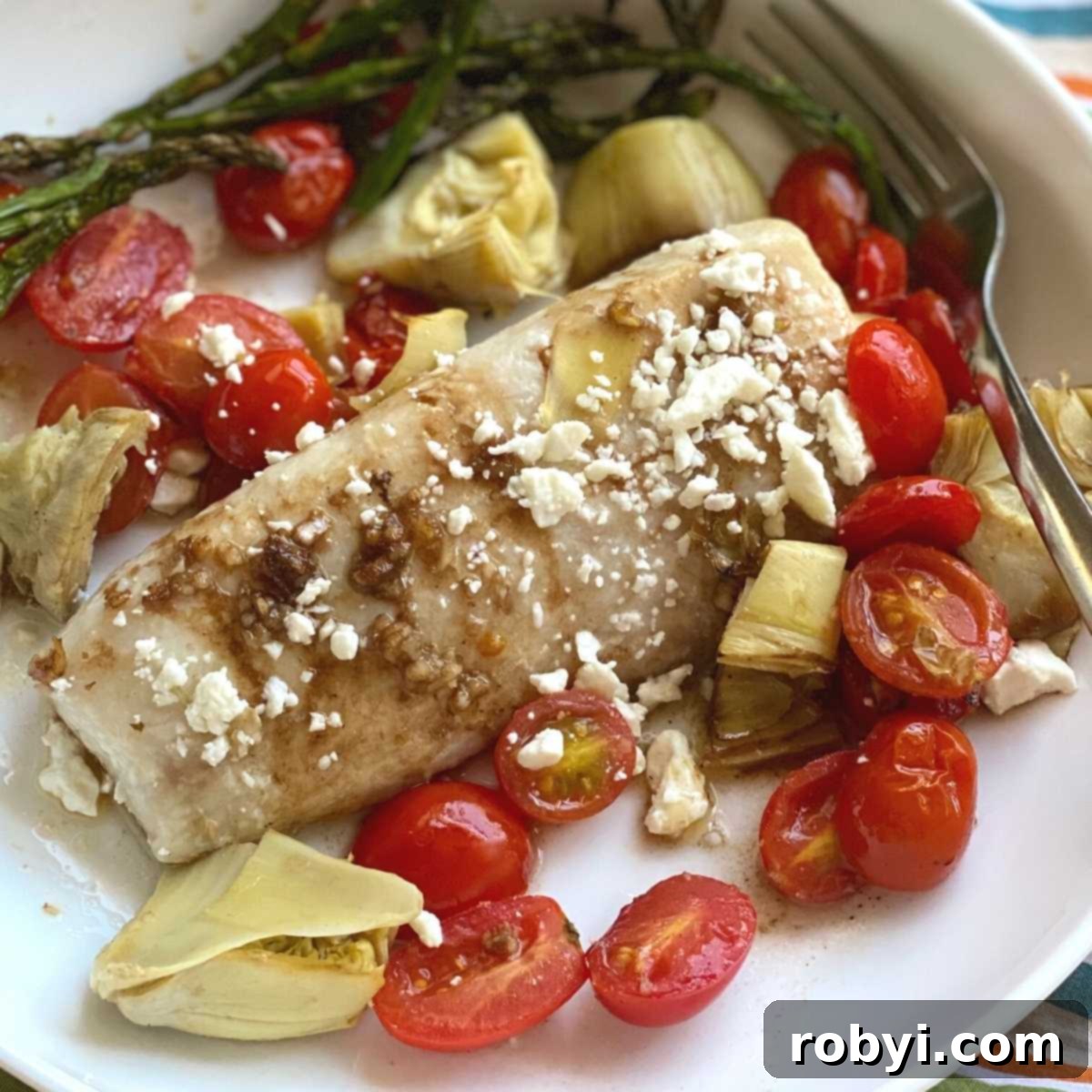 Mediterranean Baked Fish recipe on a plate with tomatoes, artichokes and feta cheese.