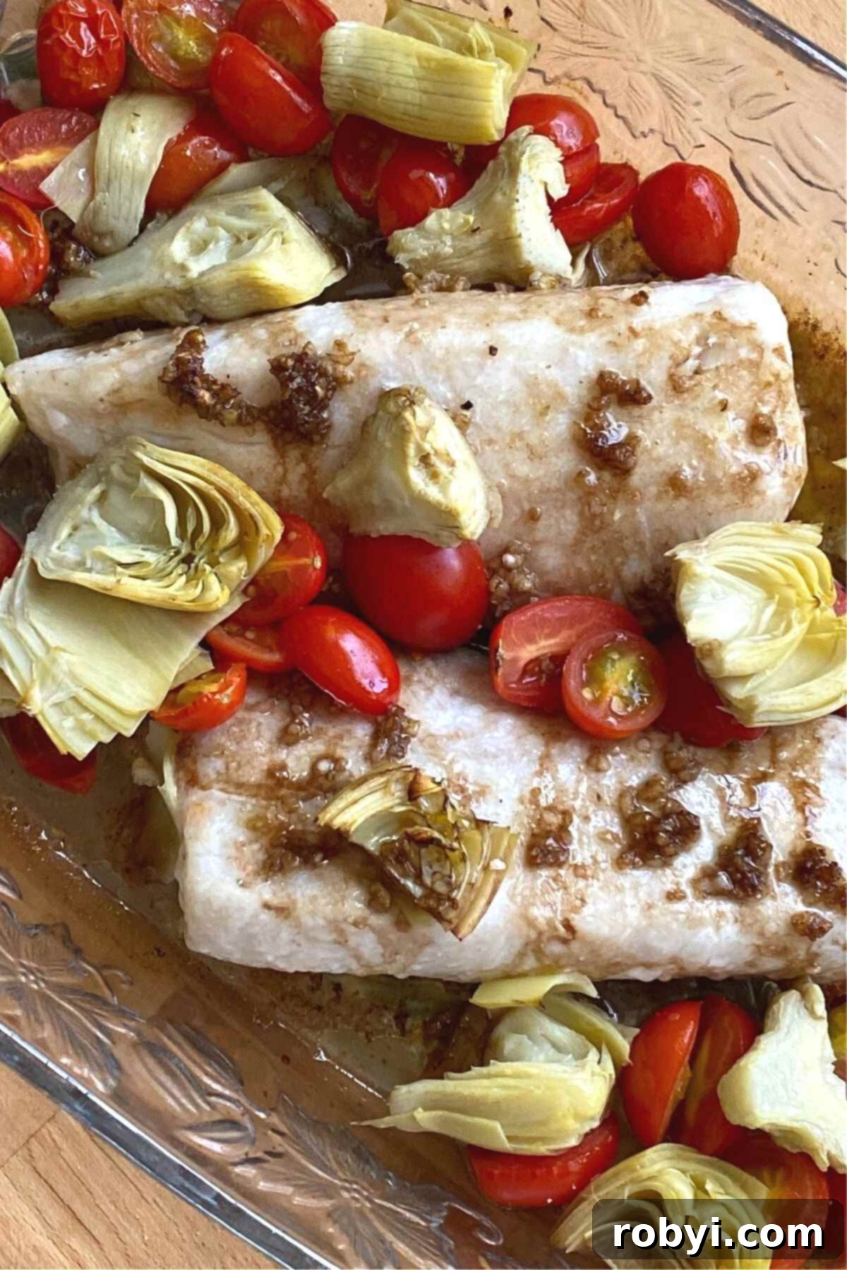 Cooked Cobia fish fillets with artichokes and tomatoes in a baking dish.