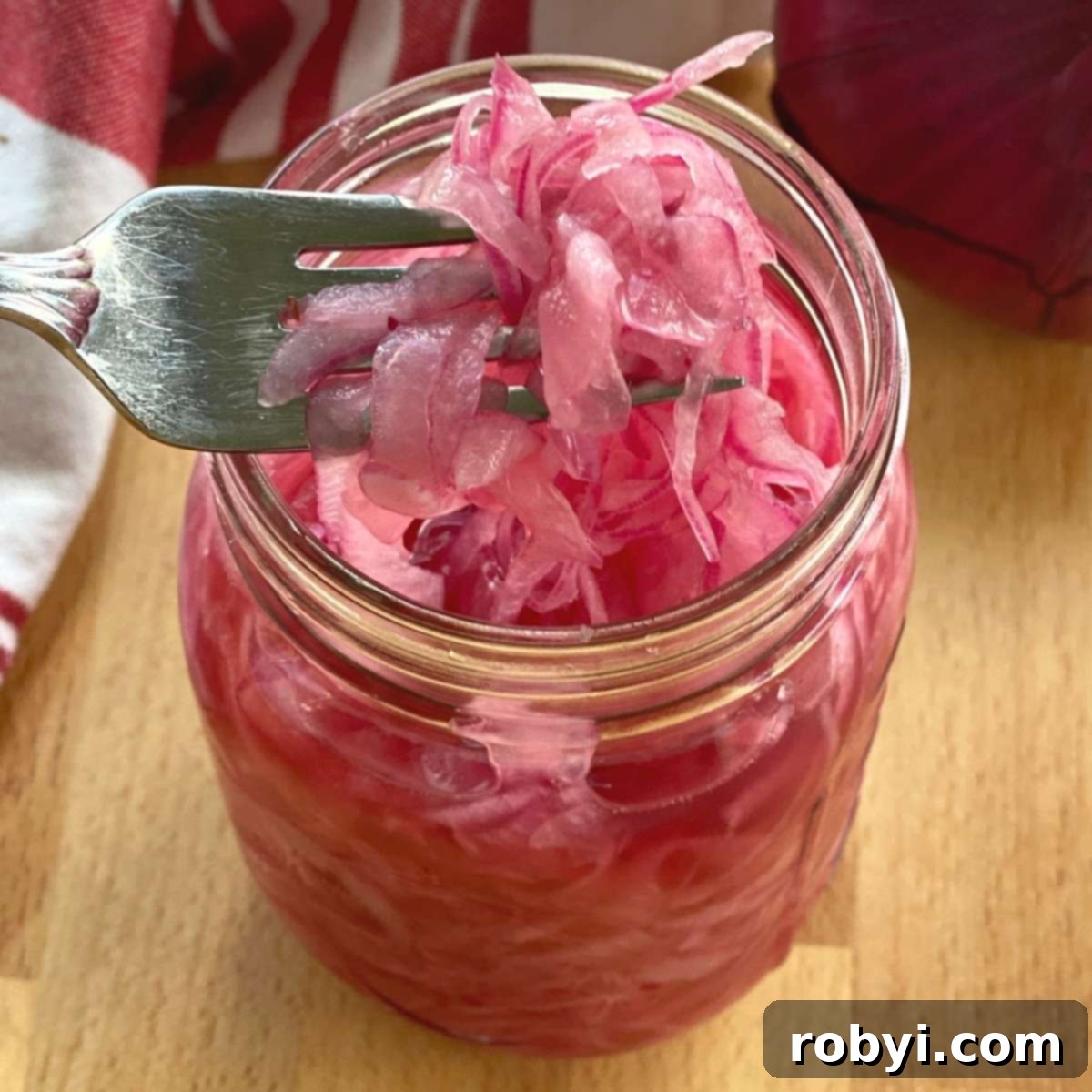 A fork lifting vibrant pink pickled onions out of a clear mason jar, showcasing their beautiful color and texture.