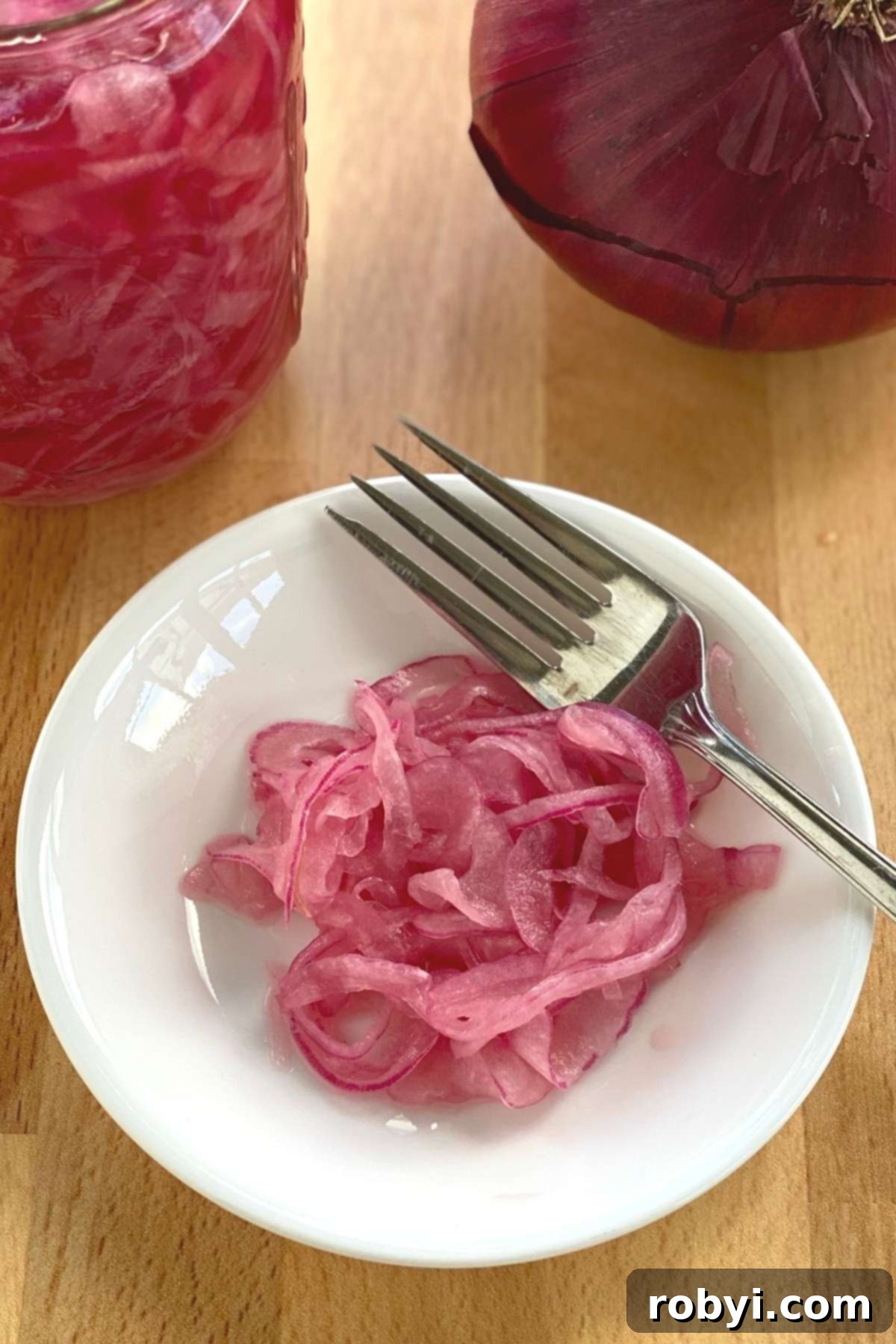 Pink pickled onions arranged artfully on a white plate with a fork.