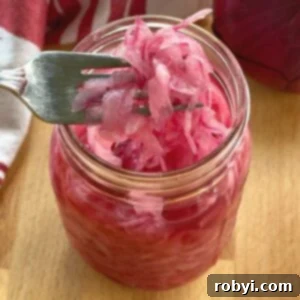 A fork lifting vibrant pink pickled onions out of a clear mason jar.