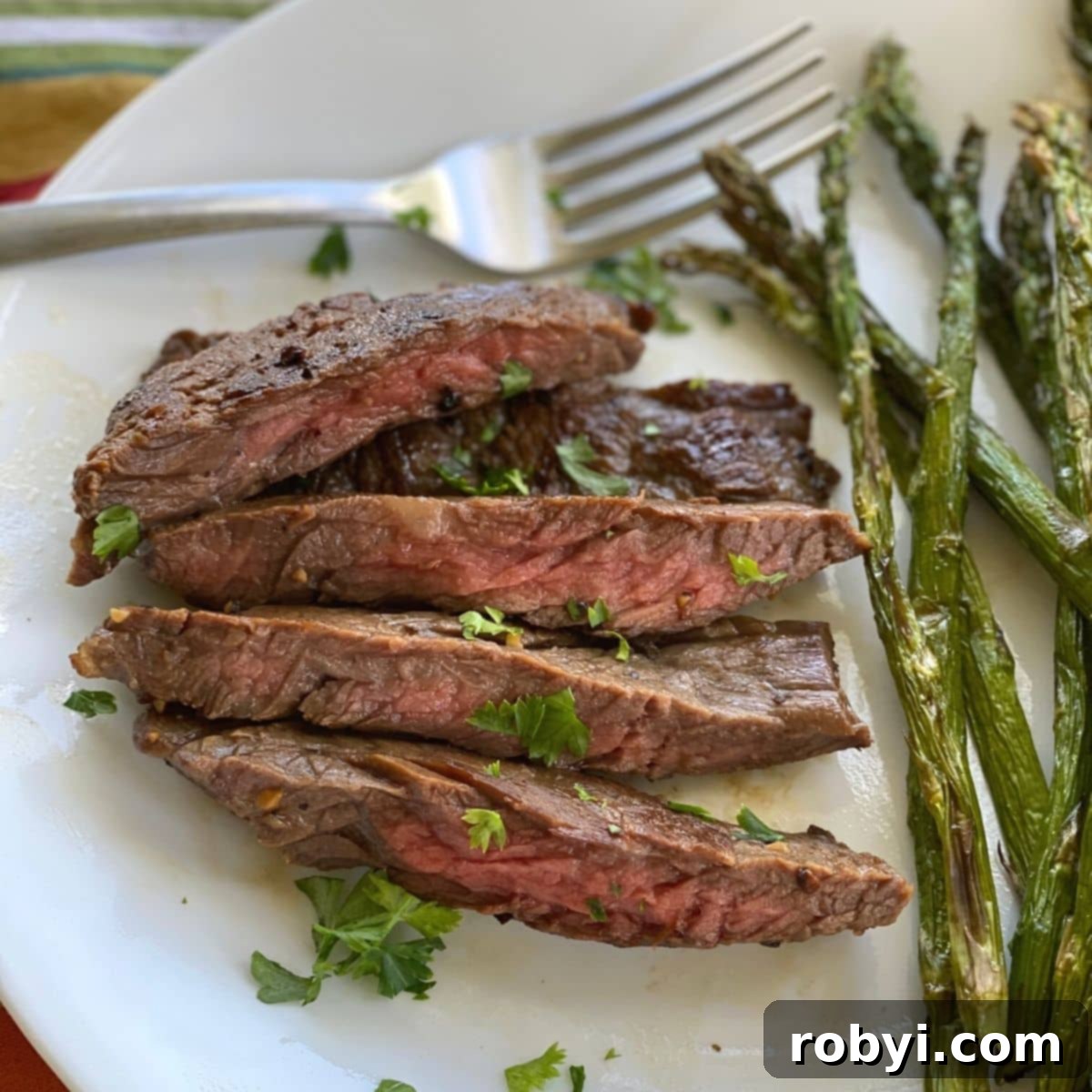 Cooked bavette steak on a plate with asparagus and fork.