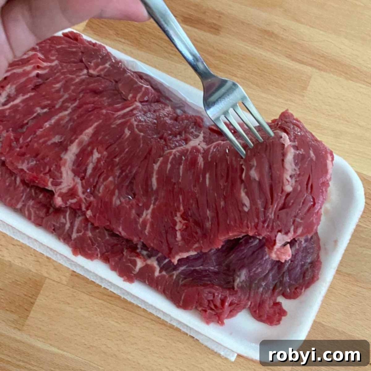 Fork lifting up a uncooked bavette steak to show marbling and loose texture.