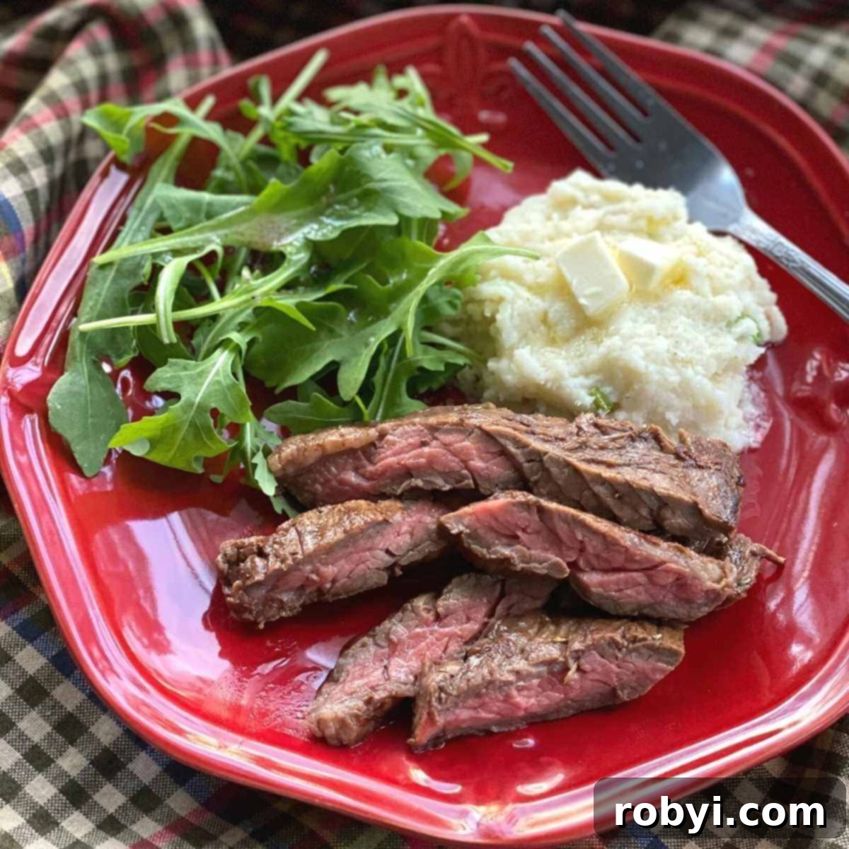Slices of bavette steak on a plate with mashed cauliflower and arugula.