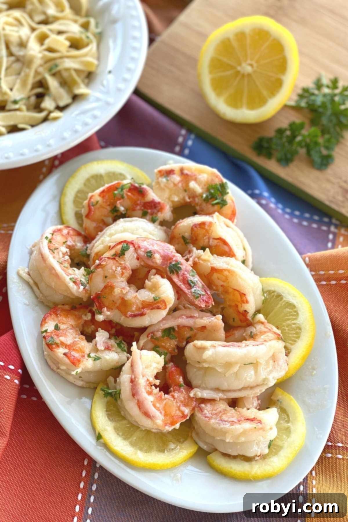 Plate of cooked colossal Argentine red shrimp in a scampi sauce on a plate surrounded by lemon slices.