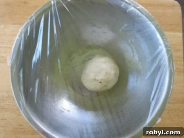 Dough for homemade pretzel bites in bowl covered with plastic wrap