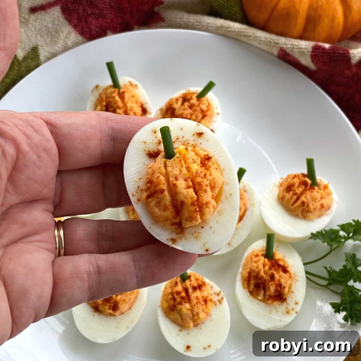 Hand holding a pumpkin deviled egg, showcasing its festive shape.