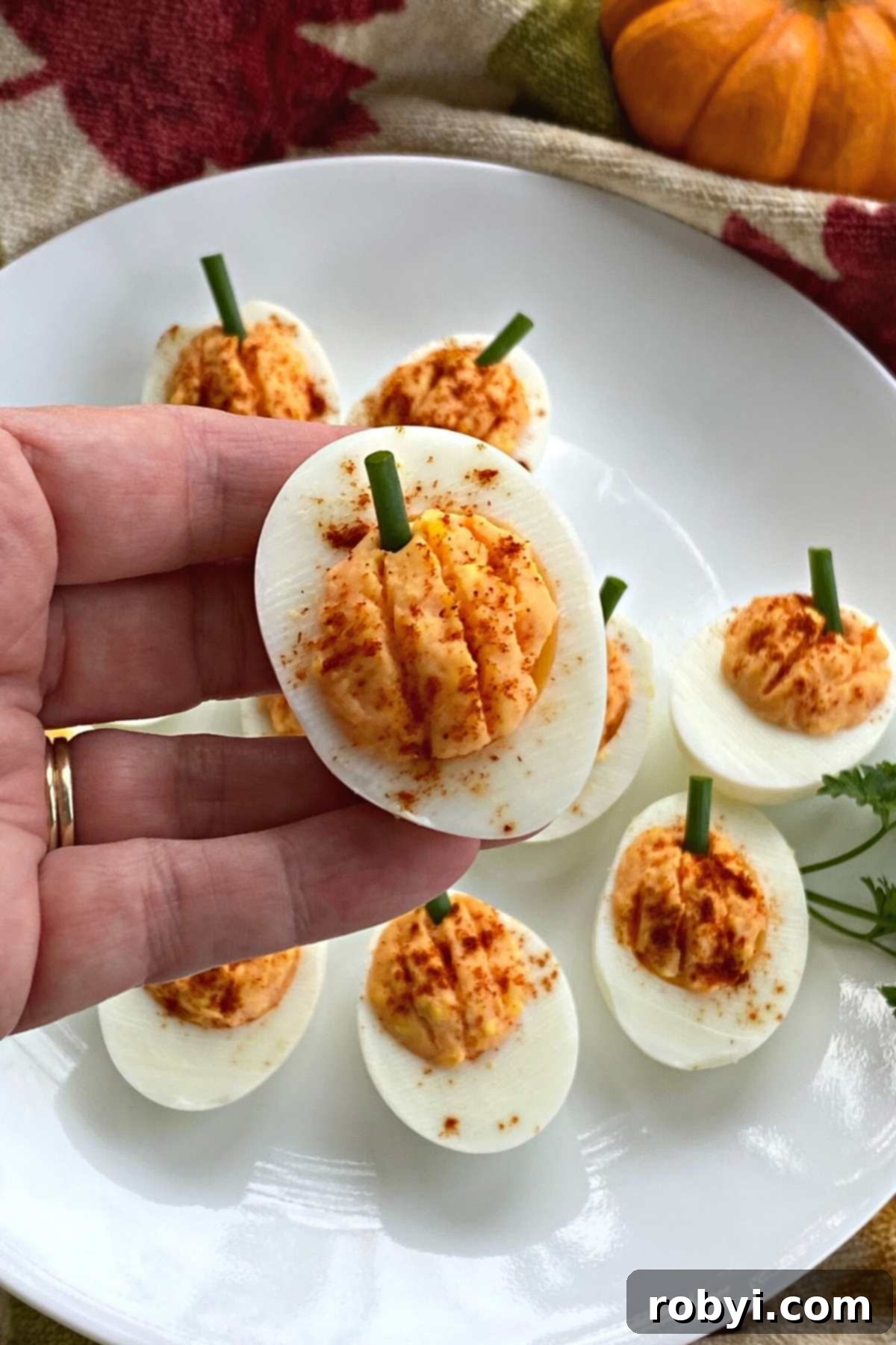 Plate of Halloween pumpkin shaped deviled eggs with a hand holding one.
