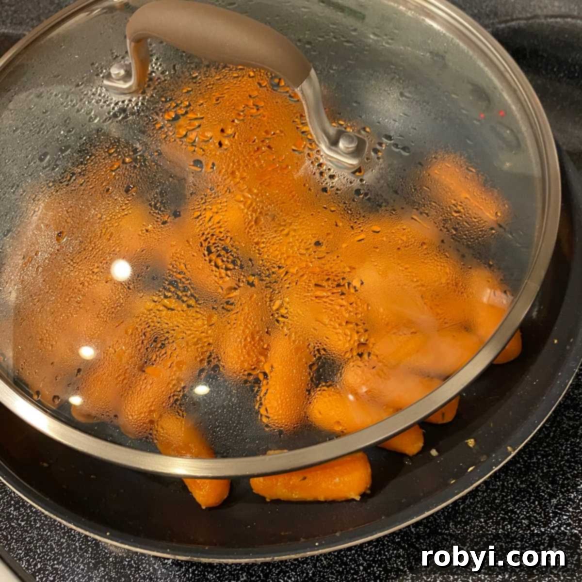 Partially covered skillet with baby carrots.