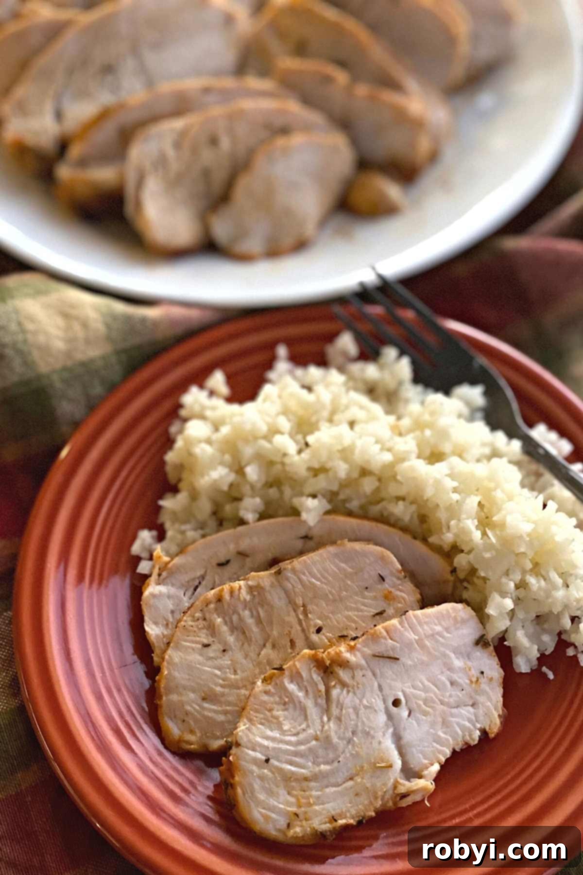 A beautifully plated baked turkey tenderloin with cauliflower rice, with a larger platter of sliced turkey visible in the background, ready to be served.