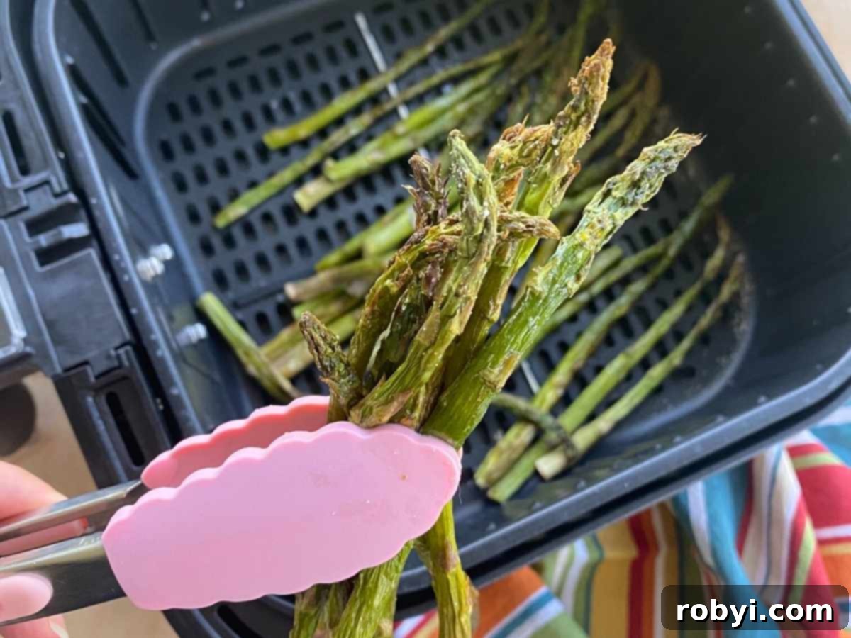 Tongs holding up roasted asparagus cooked in an air fryer.