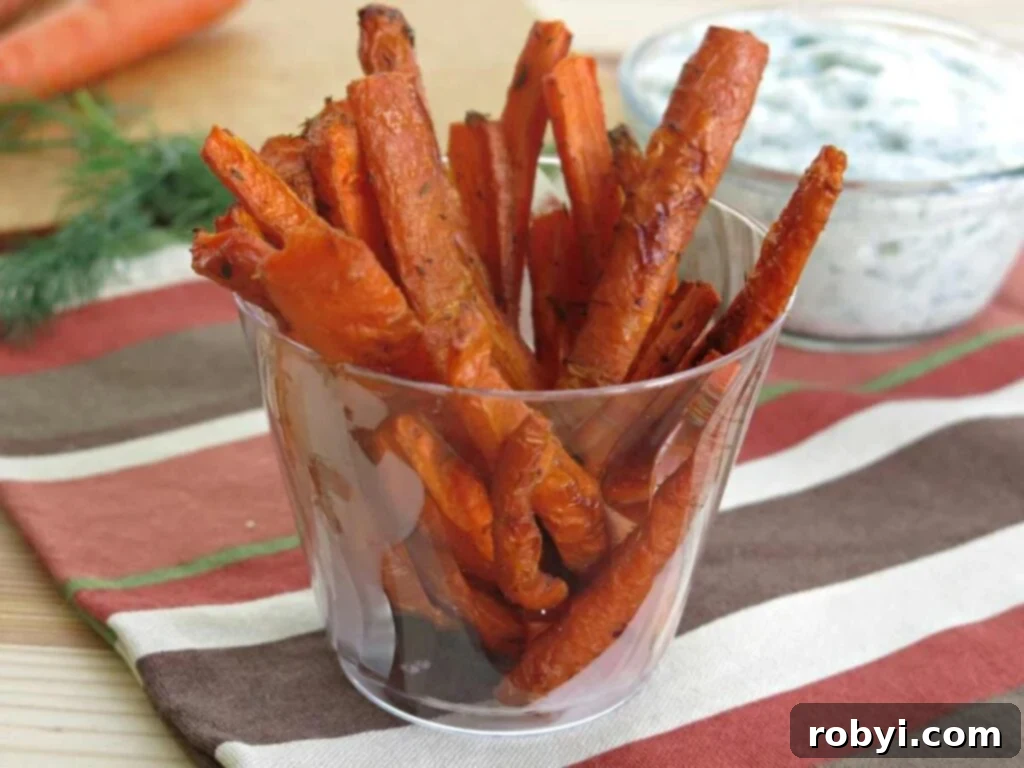 Clear cup with carrot fries stacked in it with a bowl of dip behind it.