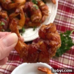 Fingers holding a stuffed bacon wrapped shrimp with more on a plate below.
