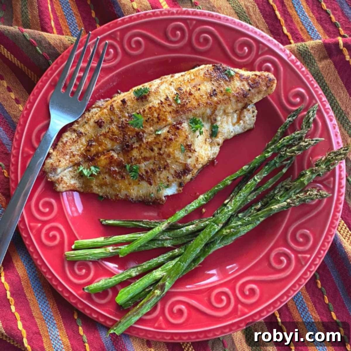 A single blackened Cajun Catfish fillet presented on a plate next to roasted asparagus spears, offering a complete healthy meal idea.