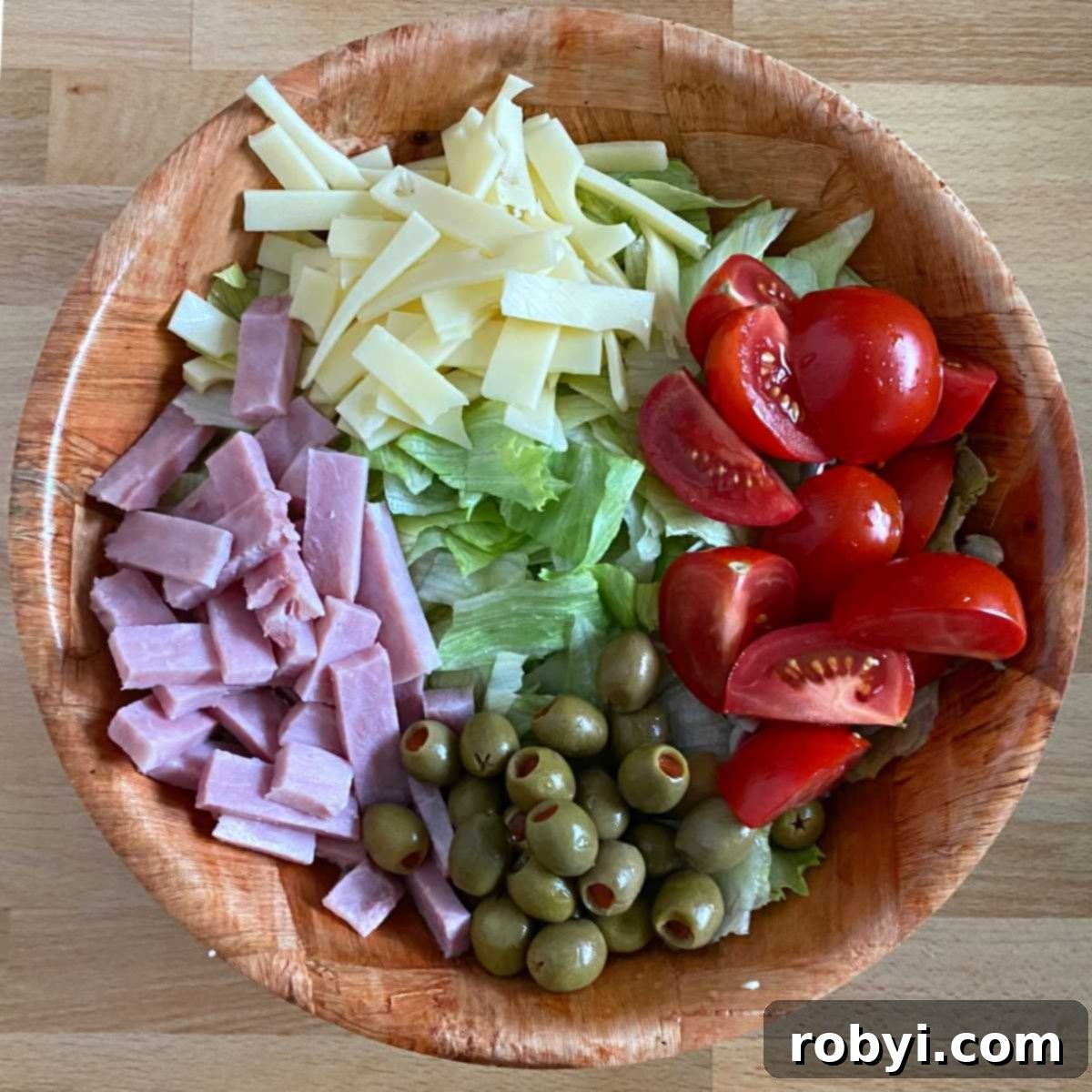 Julienned Swiss cheese and ham, wedges of tomato, green olives and lettuce in a bowl.