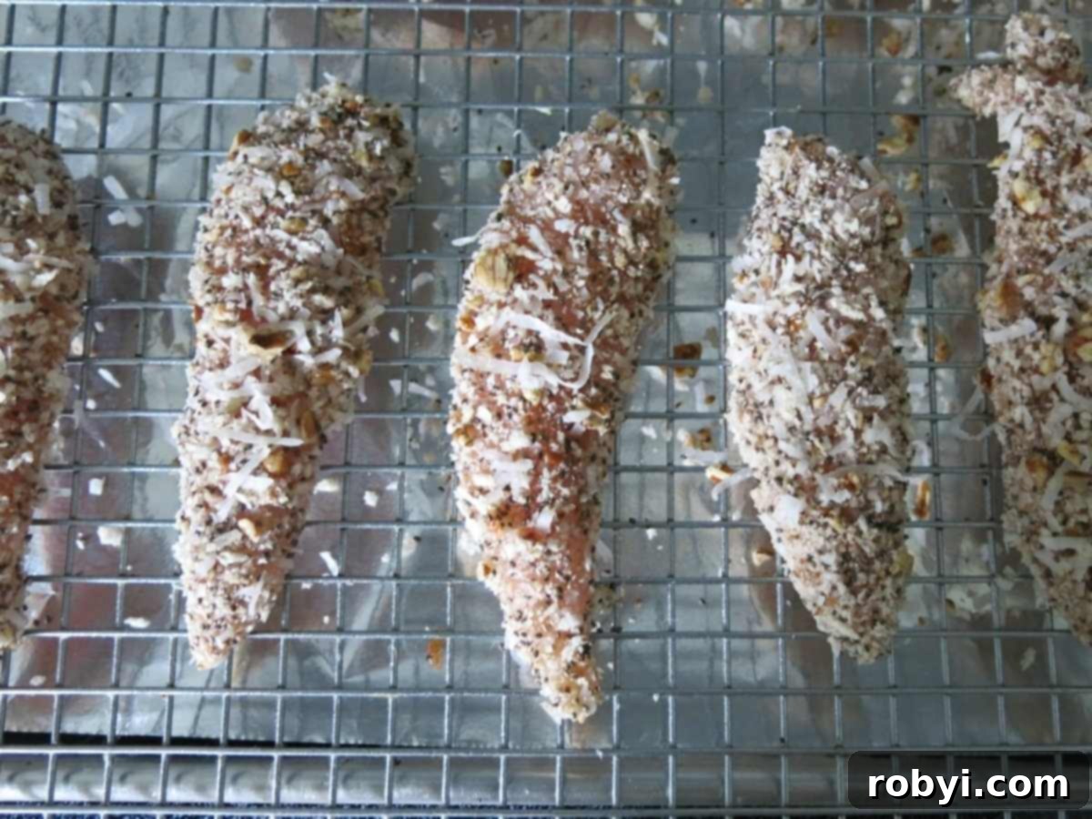 Uncooked chicken tenders with panko breading on a cooling rack placed on top of a baking sheet.