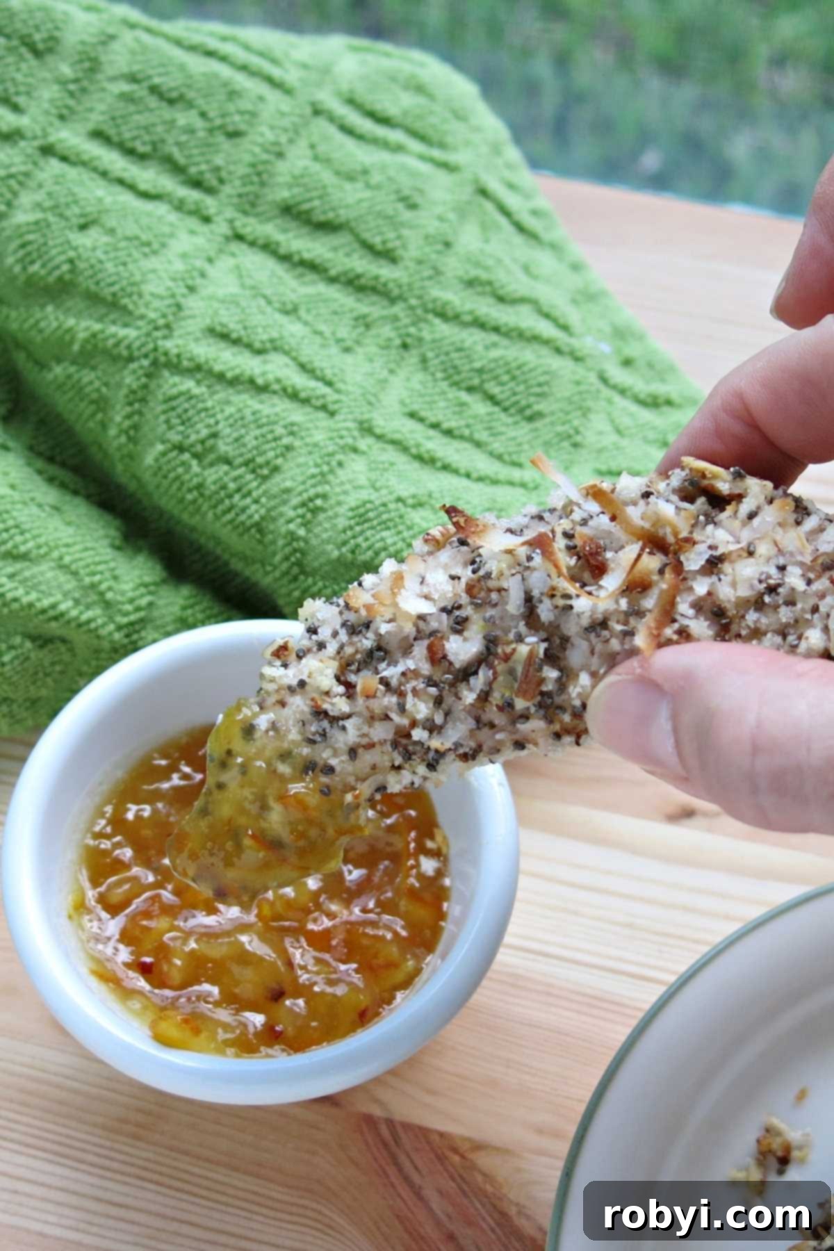 Fingers holding an easy baked chicken tender that has been dunked into a sauce.