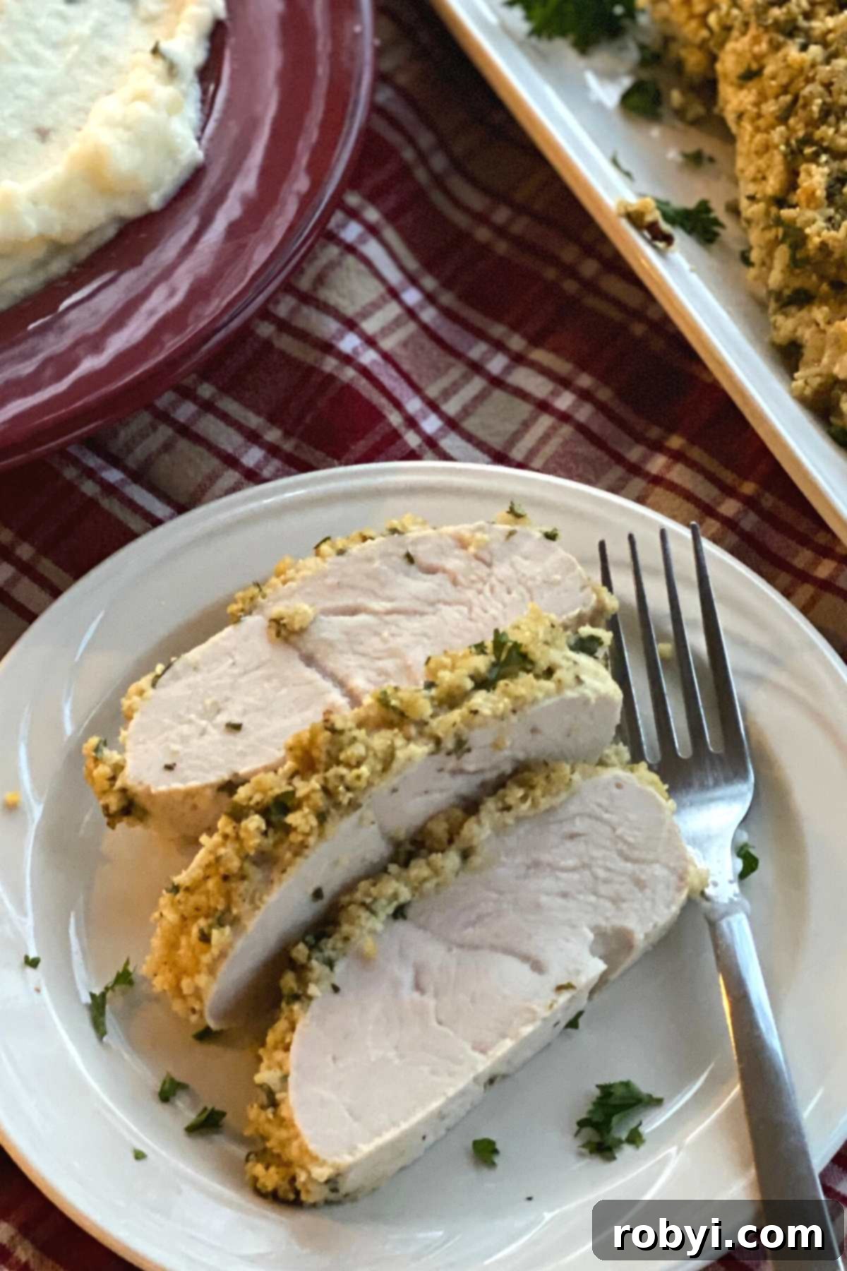 Three golden-brown slices of herb-crusted turkey tenderloins beautifully arranged on a white plate, garnished with fresh herbs, ready to be served.