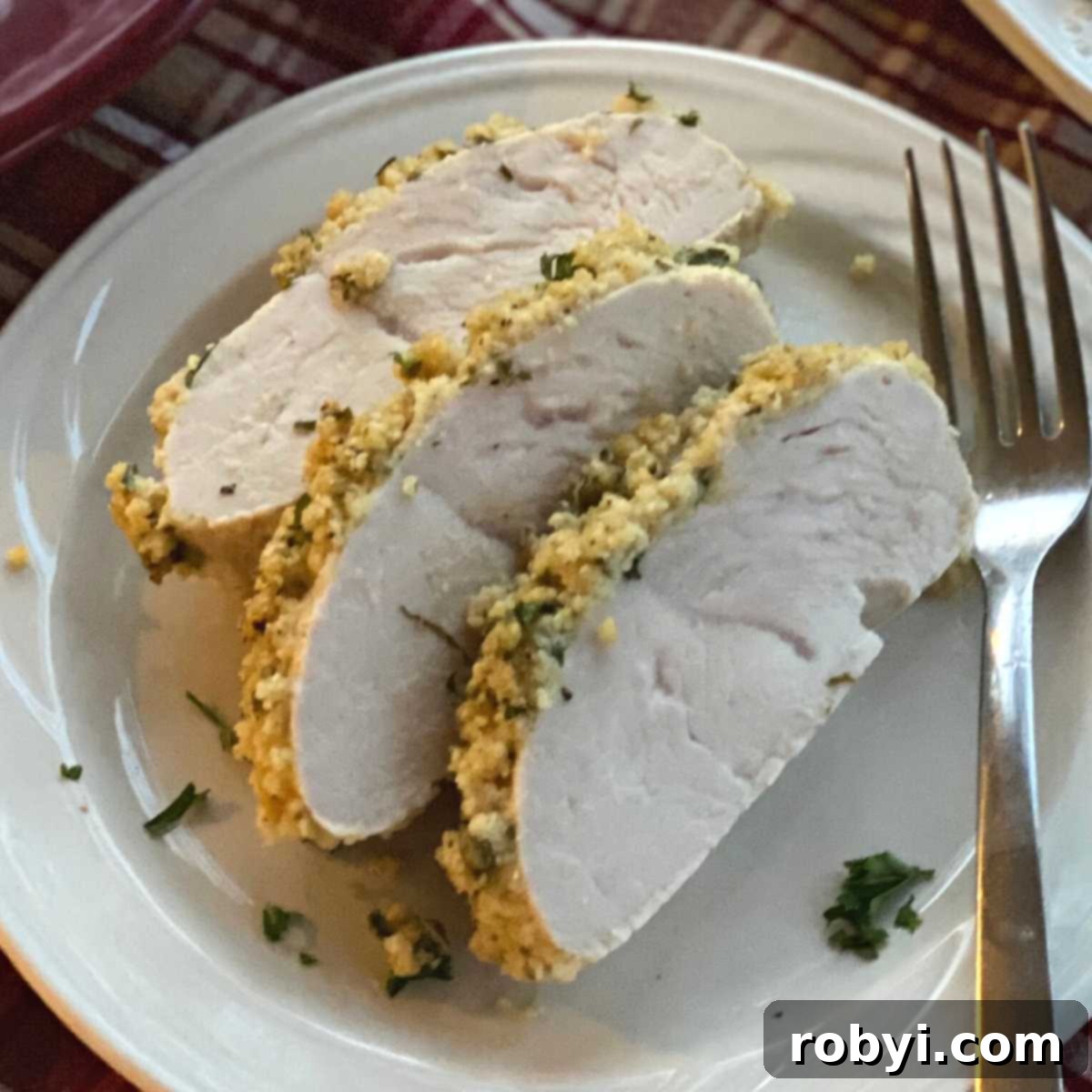 Perfectly sliced turkey tenderloin medallions with a visible herb and Parmesan crust, served on a plate with a fork, ready for a delicious meal.