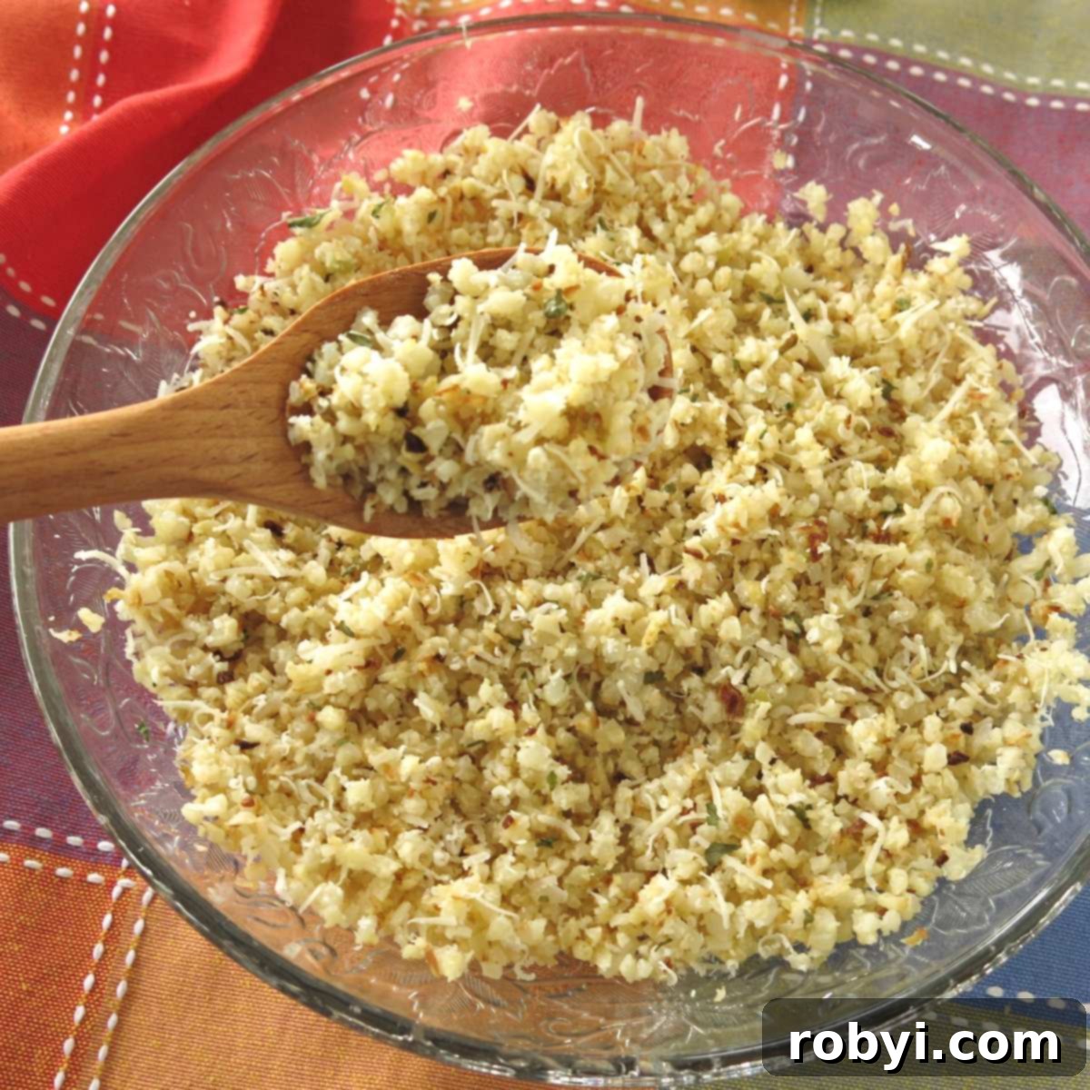 A wooden spoon lifting roasted cauliflower rice, sprinkled with Parmesan cheese, out of a bowl.