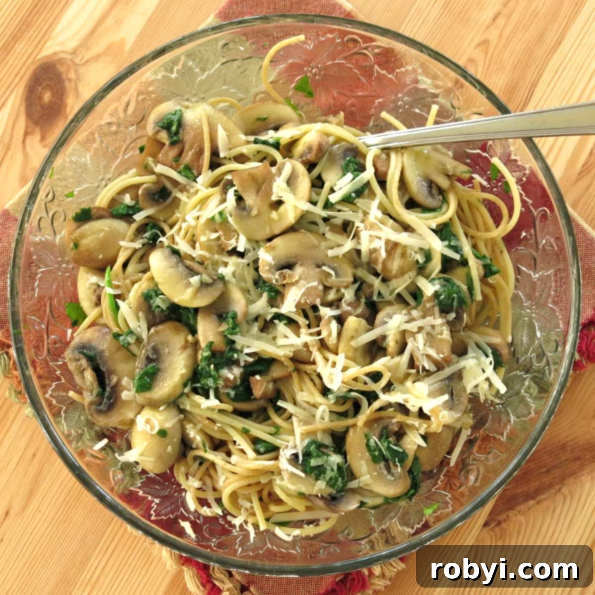 A bowl of olive oil pasta with mushrooms, fresh basil, and grated Parmesan cheese.