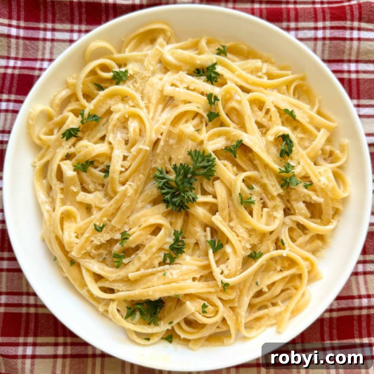 One pot fettuccine alfredo pasta on a white plate, elegantly garnished with fresh parsley and a sprinkle of Parmesan cheese.