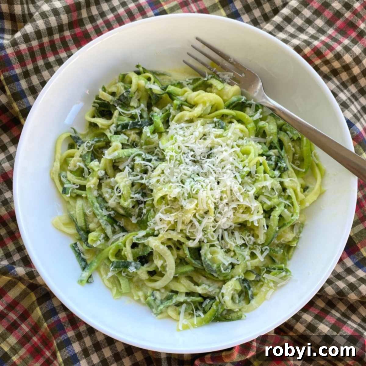 A bowl of creamy zucchini noodle alfredo with a fork, showing its delicious texture.