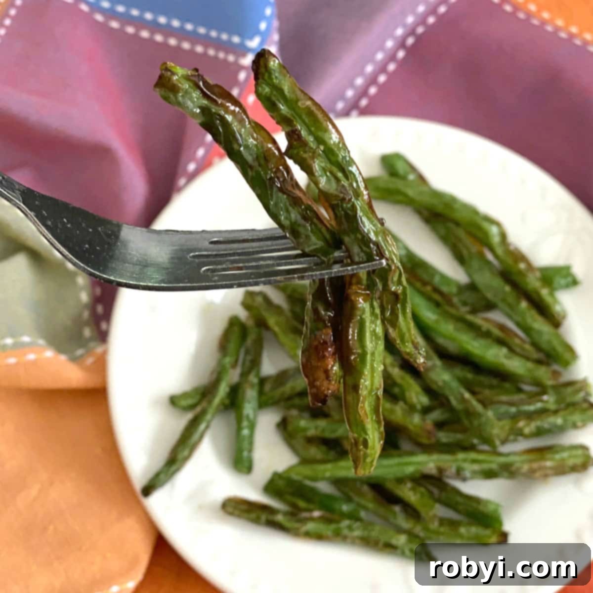 A fork holding three perfectly air-fried crispy green beans.
