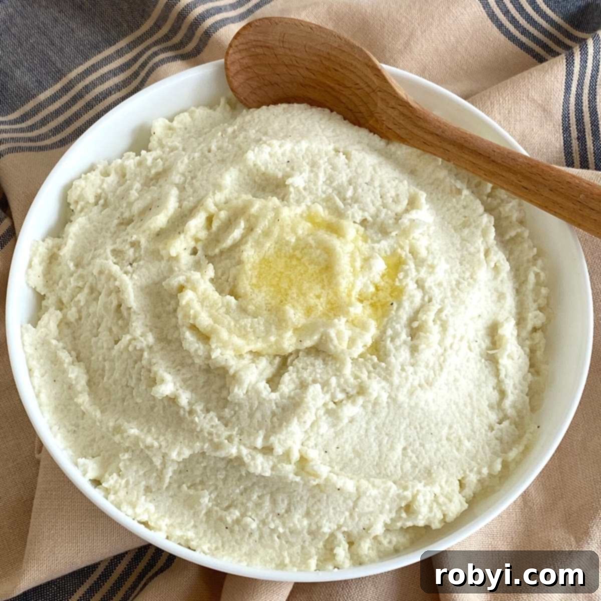 A serving bowl filled with creamy frozen cauliflower mash, with a wooden spoon resting inside.