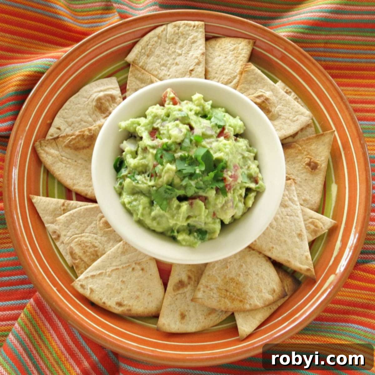 A beautifully arranged bowl of vibrant green guacamole surrounded by a generous portion of golden keto tortilla chips.