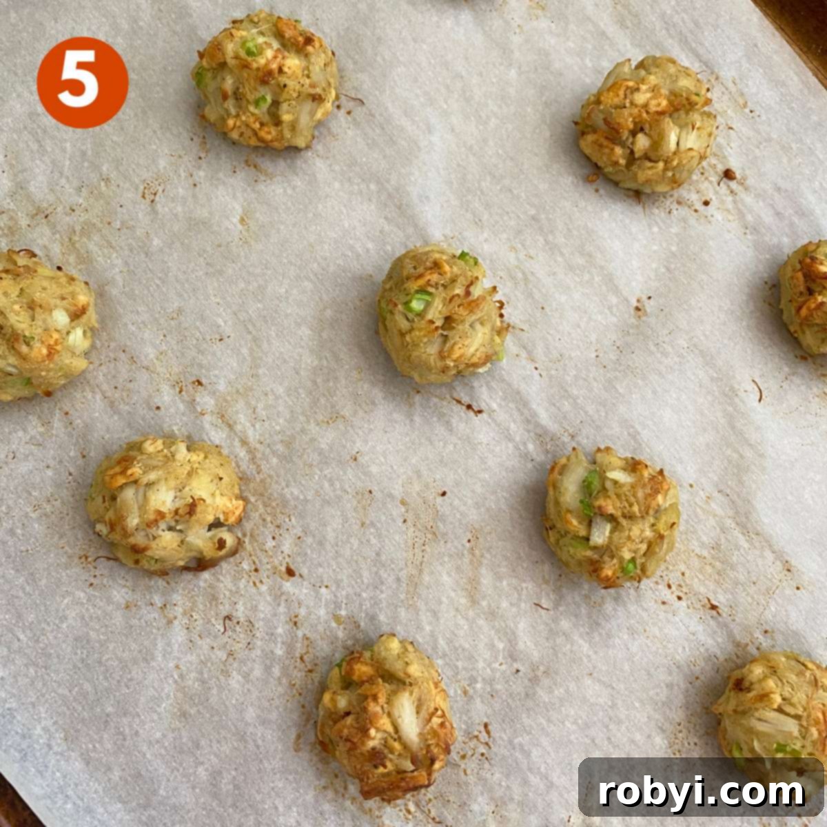 Baked crab balls arranged on a parchment-lined cookie sheet.