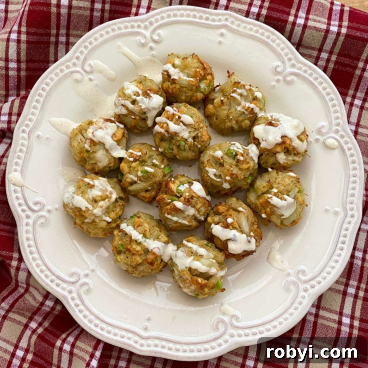 Mini crab cake bites on a plate drizzled with lemon garlic aioli, with a bowl of more crab balls and aioli behind them.