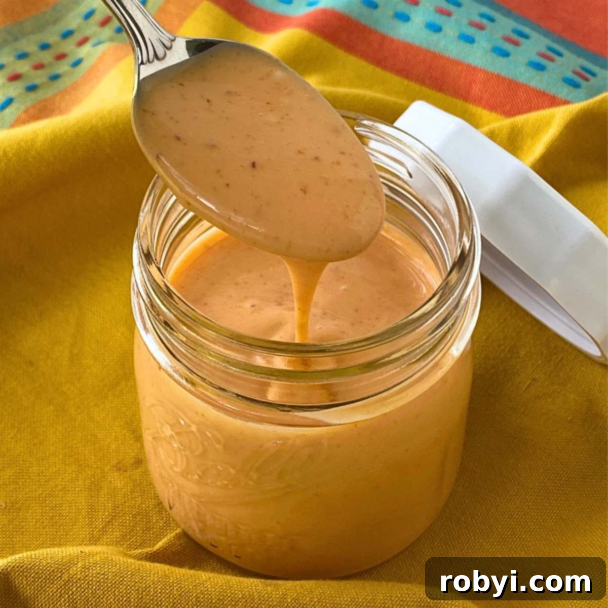 Spoon lifting homemade bang bang sauce from a small mason jar, showcasing its creamy texture.