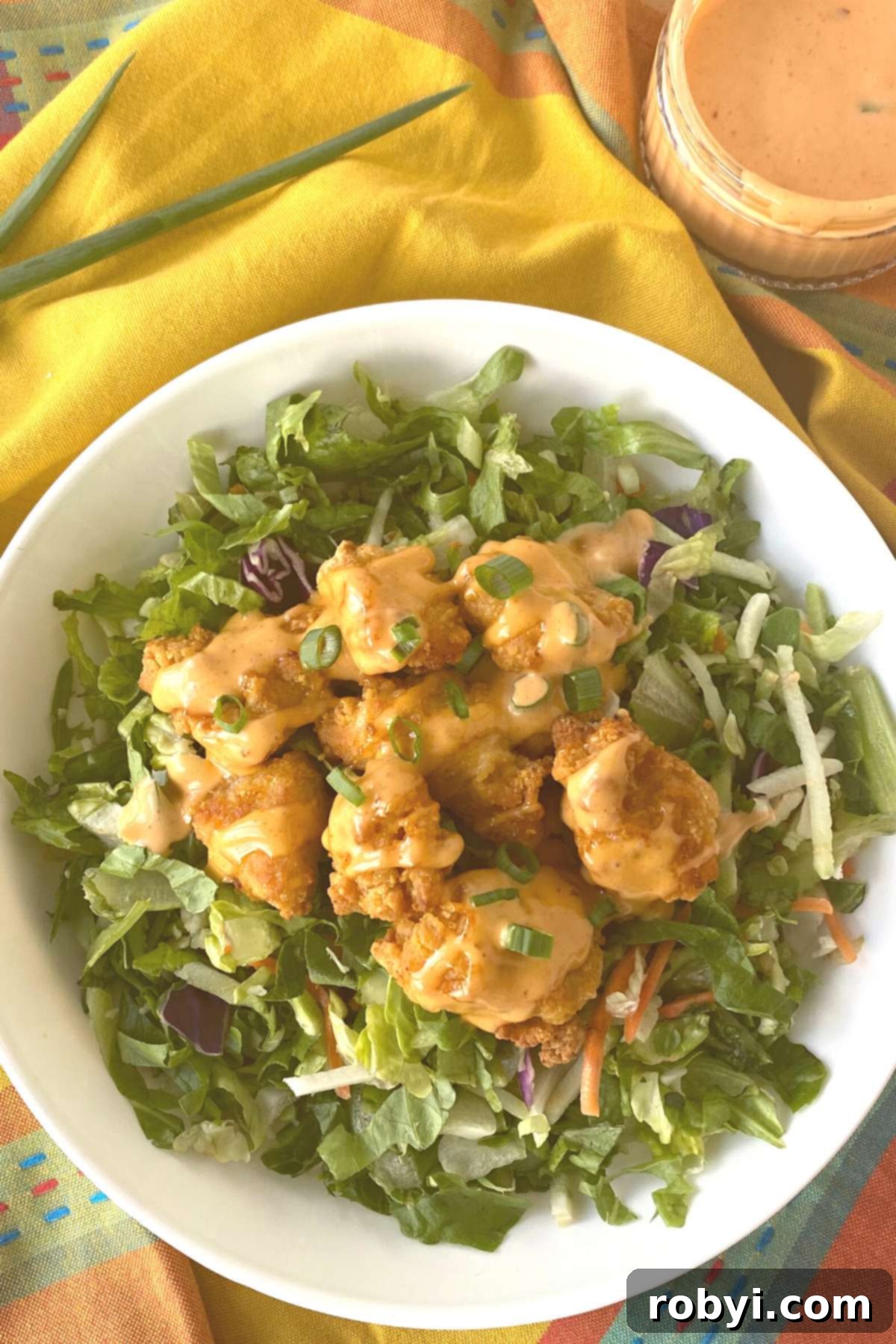 Crispy chicken nuggets covered with homemade bang bang sauce, served on a bed of fresh salad greens.