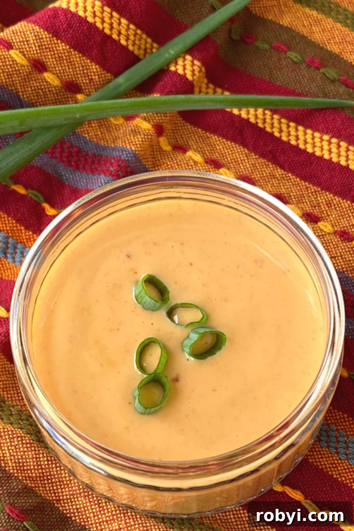 Easy homemade bang bang sauce in a small glass container, garnished with sliced green onions, with more fresh spring onions in the background.