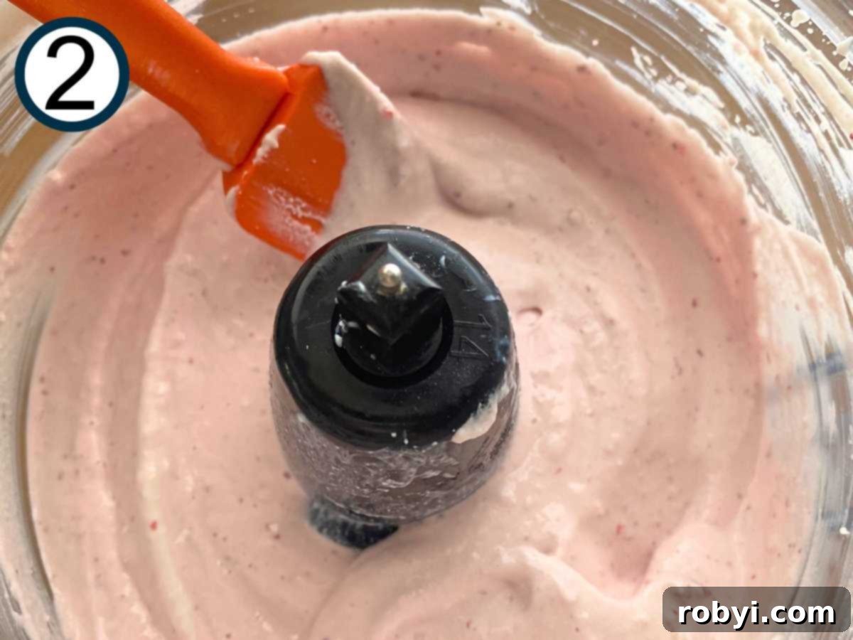 whipped cottage cheese, strawberries, vanilla extract, and sweeteners in the base of a food processor being stirred with a spatula.
