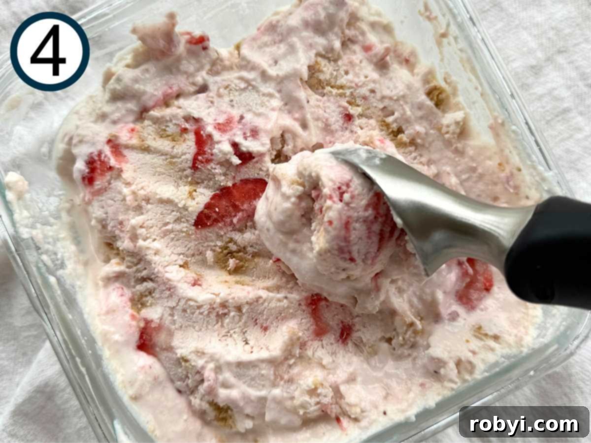 Strawberry cottage cheese ice cream being scooped with an ice cream scoop out of the glass container.