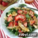 Spinach Strawberry Walnut Salad topped with chicken on a plate with walnuts and dressing in the background.
