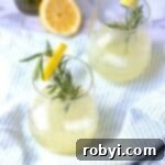 Rosemary ginger lemonade in a glass cup with a sprig of rosemary and lemon.